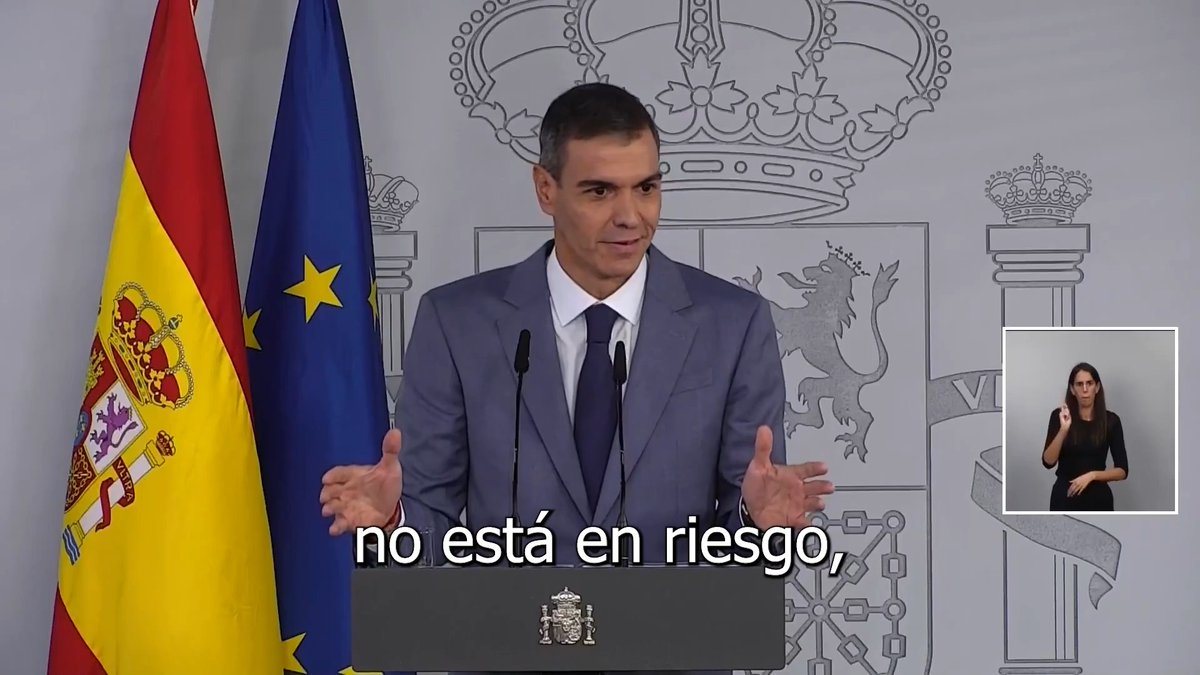 A man in a blue suit stands at a podium with the Spanish flag behind him, gesturing with his hands as he delivers a speech, with a sign language interpreter visible in the corner. The subtitle reads "no está en riesgo," and the post references a message from Spanish Prime Minister Pedro Sánchez regarding pensions, reinforcing the image's connection to his address on pension system stability.