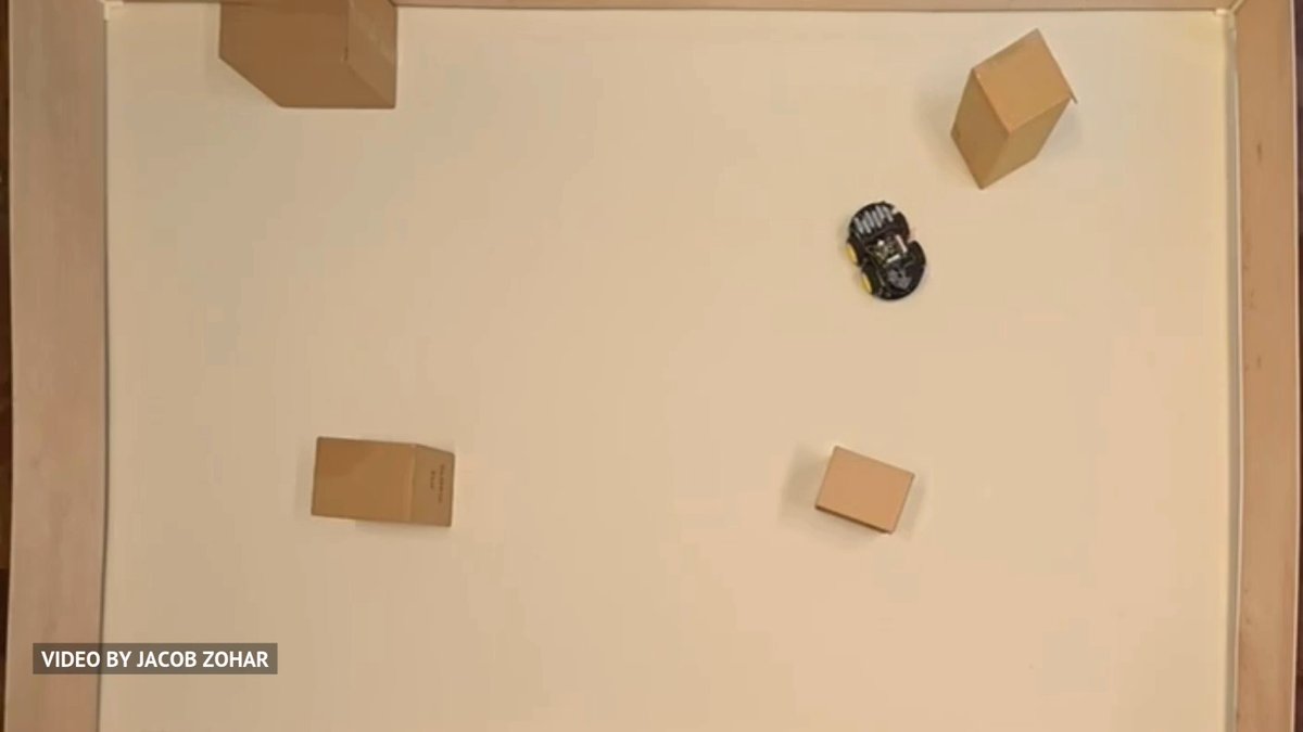 A small wheeled robot navigates a tabletop course with cardboard box obstacles, with text in the bottom left corner crediting "VIDEO BY JACOB ZOHAR".