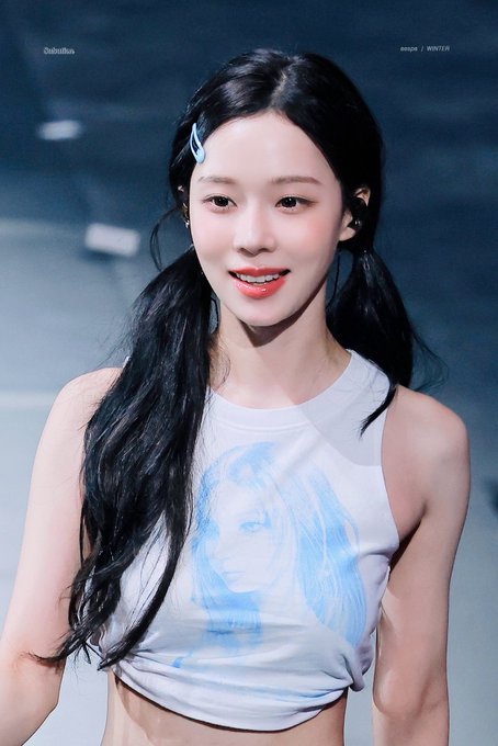 A portrait of a young Asian woman with long dark hair in pigtails, wearing a light blue sleeveless top, with small text reading 'Dubuffo' and 'aespa / WINTER' visible in the corners.