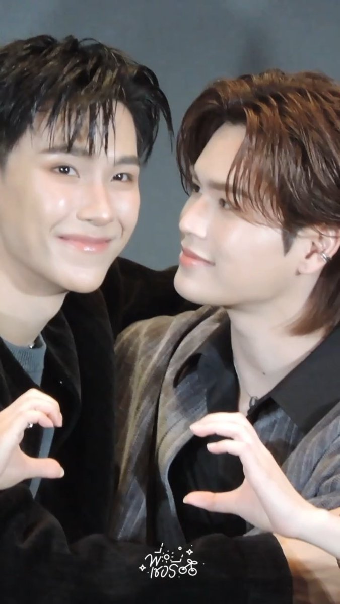 Two young men pose closely together, smiling at the camera while forming a heart shape with their hands, with the Thai text "น้องเค้าชอบพี่อิ๊ฟ" visible at the bottom of the image. The accompanying post about "#JuMarkMo1stFMinHK" and "#JuniorMark" suggests this is a moment between fans celebrating their fandom for the duo.