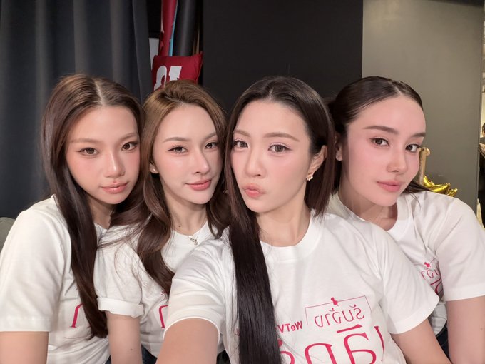 Four young women in matching white t-shirts (featuring pink text including "รับจ้าง" and "!980!") pose closely together for a selfie, likely promoting the Thai series "#รับจ้างเลิกรัก #LoveOnHireTheSeries" and inviting fans to meet them at a Saturday ticket-buying event.