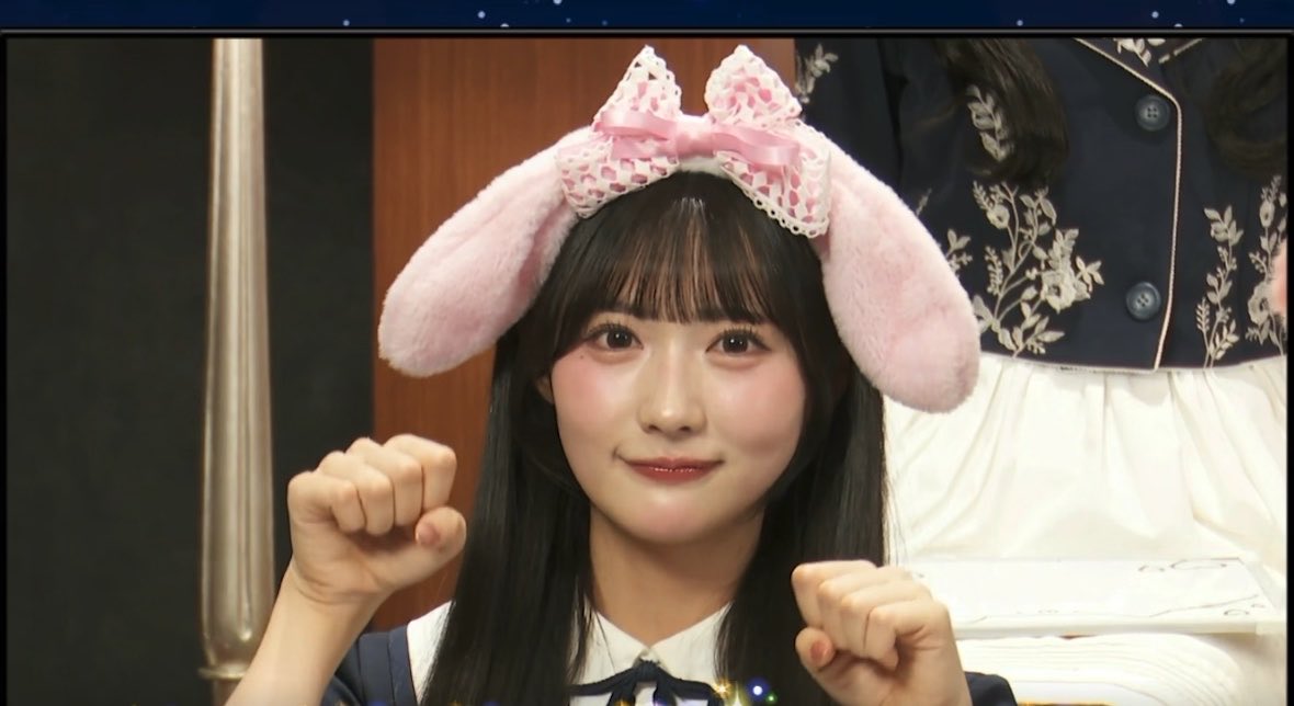 A young woman wearing a pink bunny ear hat and lace bow, holding up small fists in a cute pose.