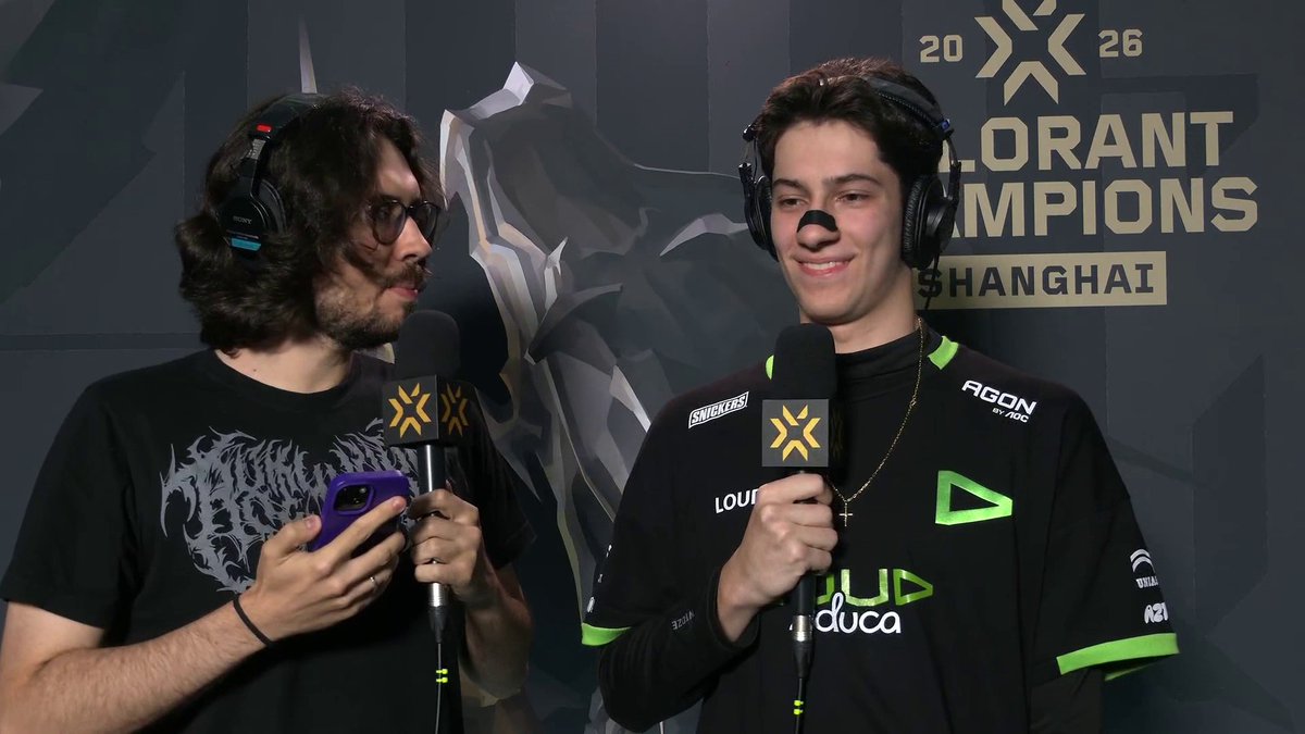 Two commentators wearing headsets conduct a post-match interview at VALORANT Champions 2026 in Shanghai, with the event branding visible in the background. The interviewee wears a black and green jersey with "LOUD" and sponsor logos, holding a Valorant-branded microphone while smiling during the interview.