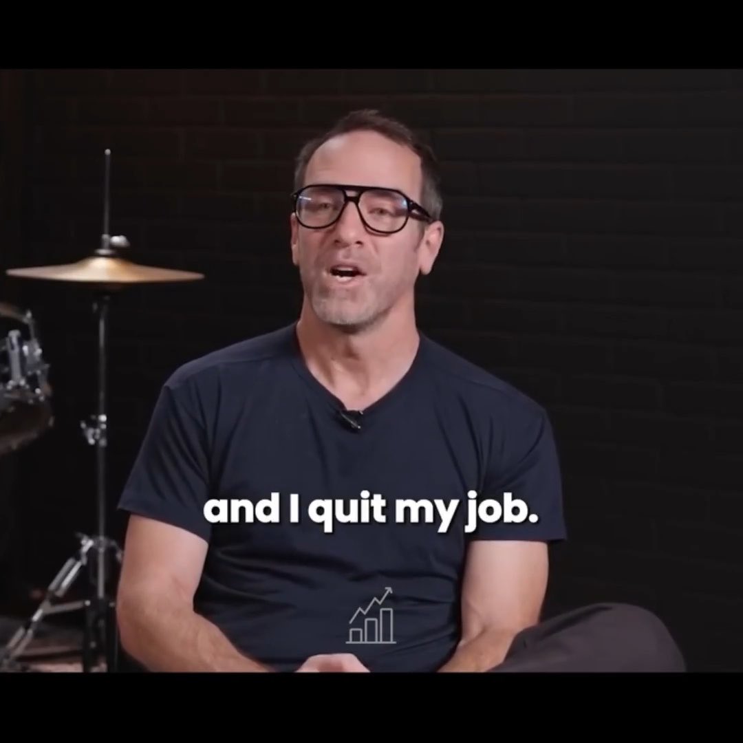 A screenshot from a video showing a middle-aged man wearing glasses and a dark v-neck t-shirt sitting in front of a drum kit, with the subtitle 'and I quit my job.' displayed below him.