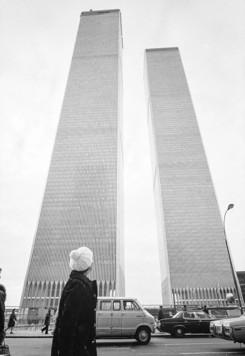 HistoryCalendar's tweet photo. A woman looking up at the Twin Towers of the World Trade Center in Manhattan, photographed just months after the complex was officially completed in April 1973. https://t.co/wBriQGtAks