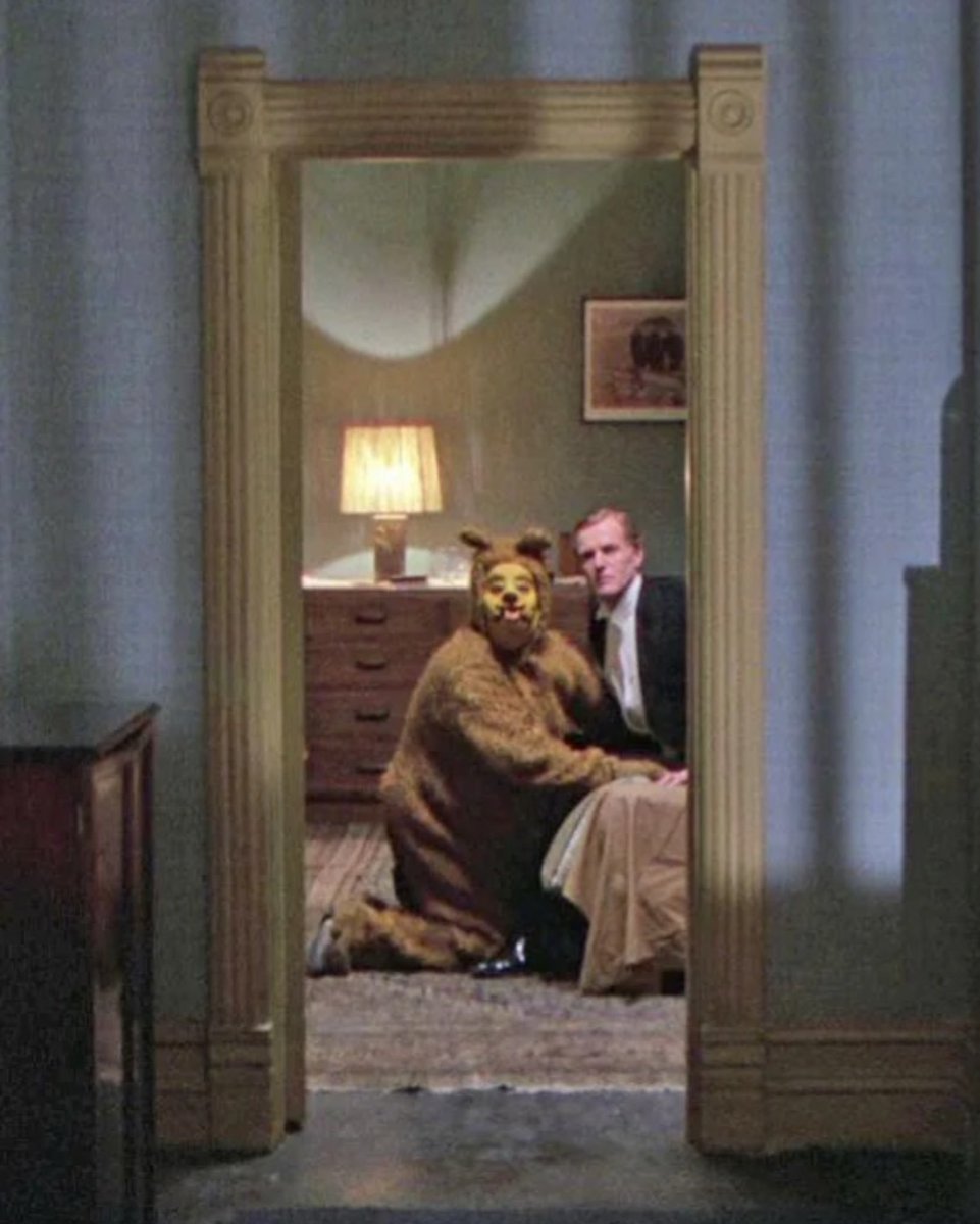 creepydotorg's tweet photo. This is one of the strangest images in movie history, and “The Shinning” never explains it. To understand it, you have to go back to Stephen King's book. 

Years earlier, the hotel belonged to Horace Derwent, a rich and powerful man. Roger was his lover, and he would do anything to please him.

One night, at a costume party, Derwent decided to humiliate Roger in front of everyone. He made him wear a dog costume, crawl on the floor, and do tricks like a pet. If Roger obeyed, Derwent promised, they would spend the night together.

That cruel night never left the hotel. It became one of its many ghosts. When Kubrick made the film, he turned the dog into a bear and cut almost the whole story, leaving only that disturbing moment.