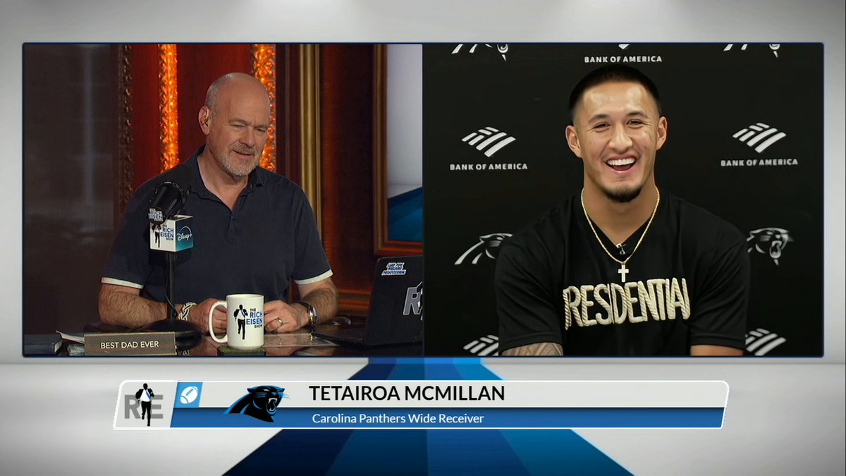 A bald man sits at a desk with a microphone branded "The Rich Eisen Show," speaking via video call with Tetairoa McMillan, a smiling Carolina Panthers Wide Receiver wearing a black "ESSENTIALS" shirt and cross necklace, appearing in front of a Bank of America backdrop. The chyron displays "TETAIROA MCMILLAN, Carolina Panthers Wide Receiver," as the caption captures McMillan downplaying his vocal presence during games.