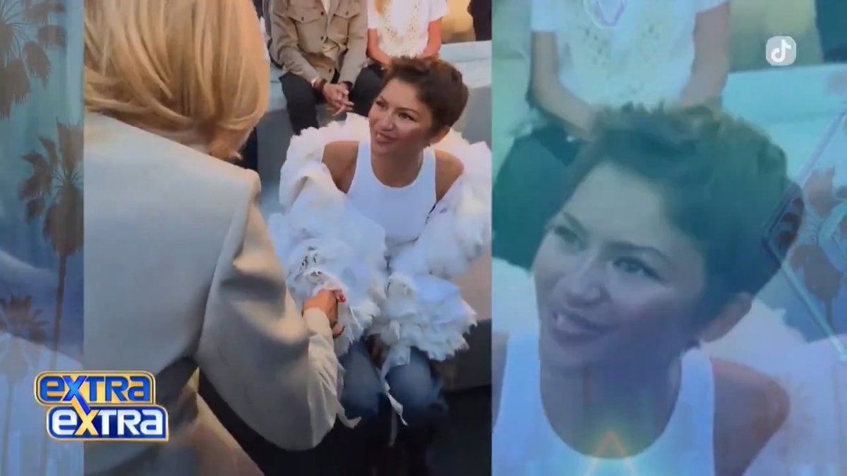 A split-screen entertainment news clip from "Extra Extra" showing a woman with short hair in a white top and feathered shawl being interviewed, alongside a TikTok video of the same woman.