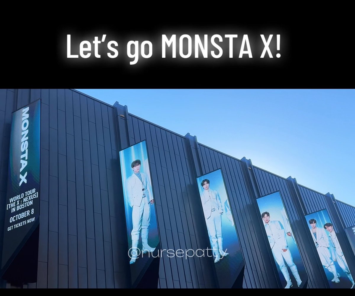 Photograph of a building exterior featuring multiple billboards advertising 'MONSTA X WORLD TOUR [THE X : NEXUS] IN BOSTON OCTOBER 8' with the caption 'Let's go MONSTA X!'.