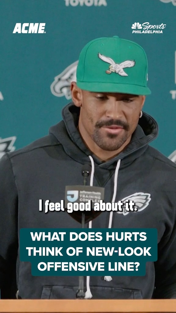 Jalen Hurts, wearing a green Eagles cap and dark hoodie, stands at a podium at the Jefferson Health Training Complex with the caption "I feel good about it." responding to a question about the Eagles' new-look offensive line, as shown by the "WHAT DOES HURTS THINK OF NEW-LOOK OFFENSIVE LINE?" text overlay. The NBC Sports Philadelphia and ACME logos appear in the corners.