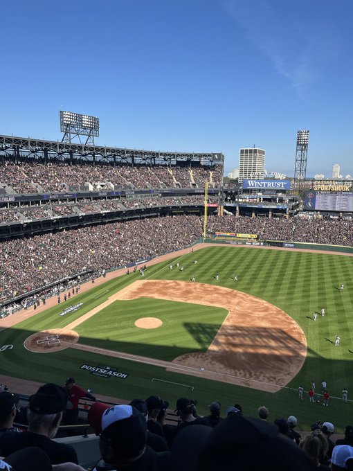 An elevated view of a packed baseball stadium during a game, showing the field, players, and crowds under a clear blue sky.