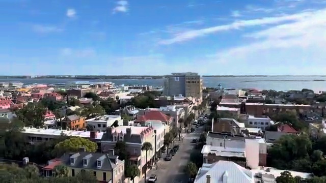 An aerial view of a coastal town with buildings and a waterfront under a partly cloudy sky.
