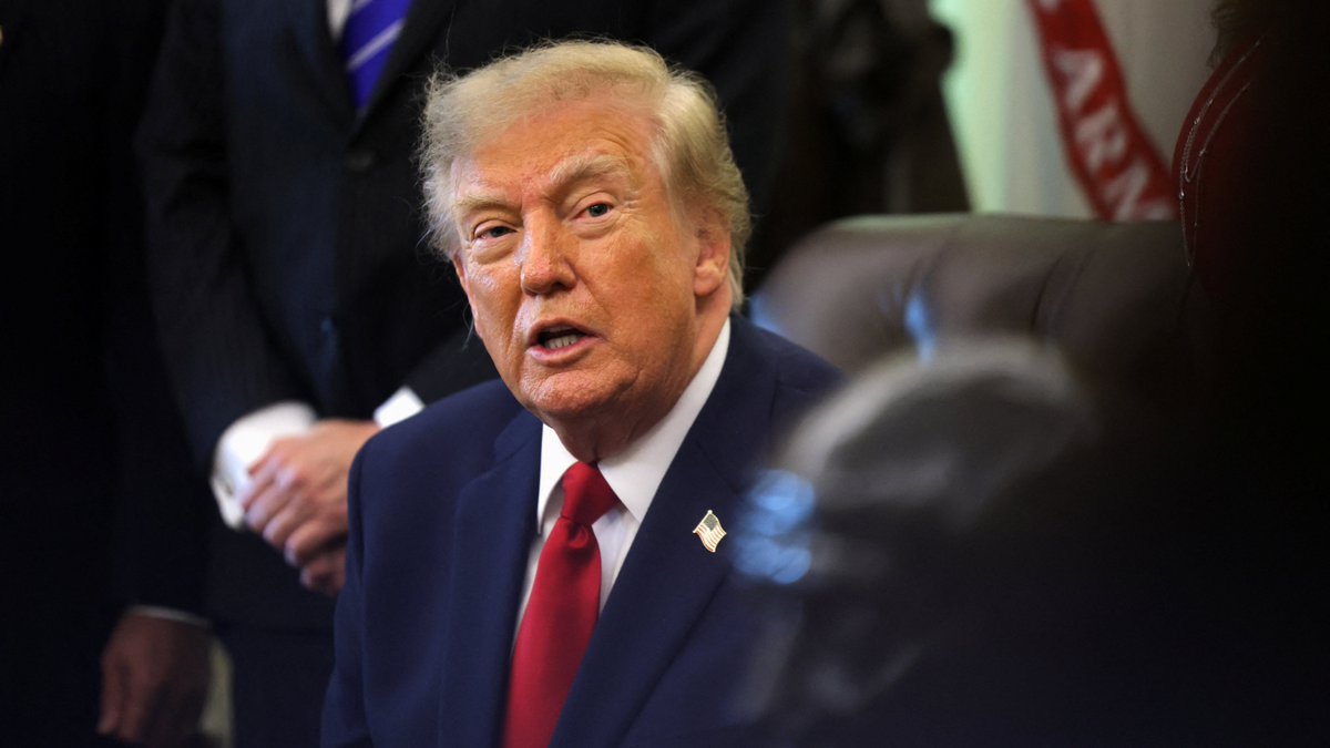 Donald Trump, wearing a navy suit and red tie with an American flag pin, is seen speaking with his mouth open, seemingly addressing the media about Russia's reported containment of a situation involving a lab worker's death.