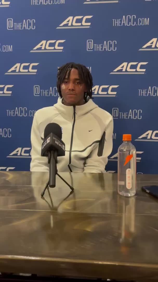 A young athlete with braided hair sits at a press conference table in front of an ACC-branded backdrop, wearing a white Nike jacket with a microphone and a Gatorade bottle nearby.