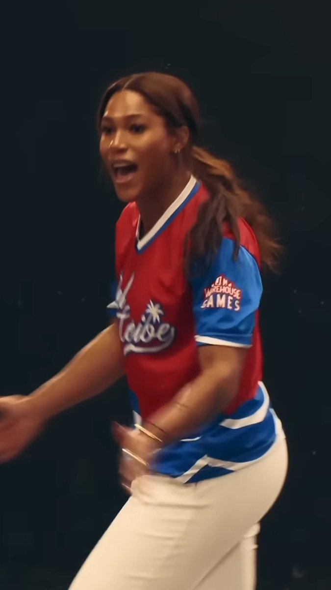A woman wearing a red and blue 'Oh Warehouse Games' jersey and white pants is shown with an excited expression.
