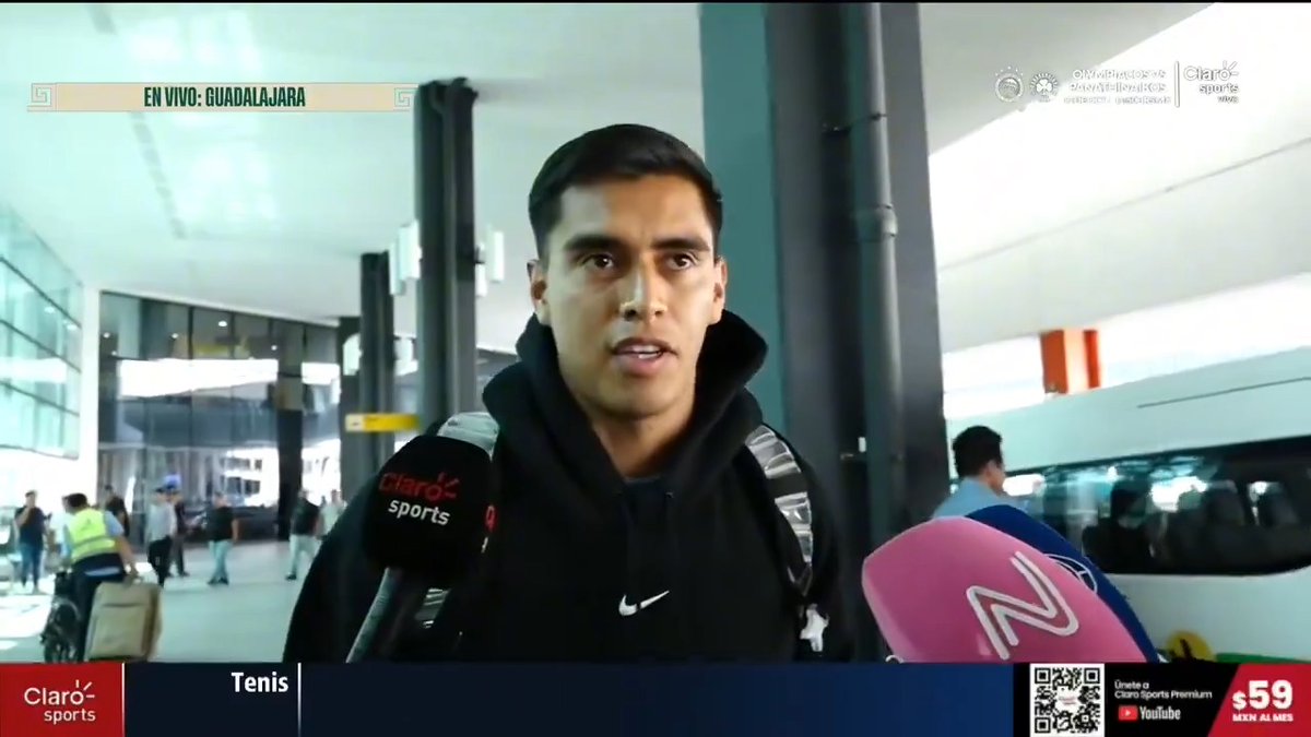 A screenshot from a Claro Sports news broadcast ('EN VIVO: GUADALAJARA') showing a man in a black Nike hoodie being interviewed in what appears to be an airport terminal, with sports microphones in the foreground.
