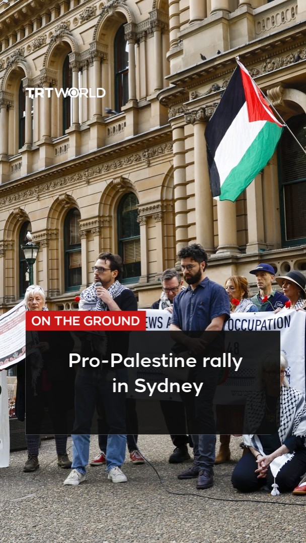 A screenshot from TRT World titled 'ON THE GROUND: Pro-Palestine rally in Sydney,' showing demonstrators standing before a classical building with a Palestinian flag and a banner referencing 'Jews Against the Occupation'.