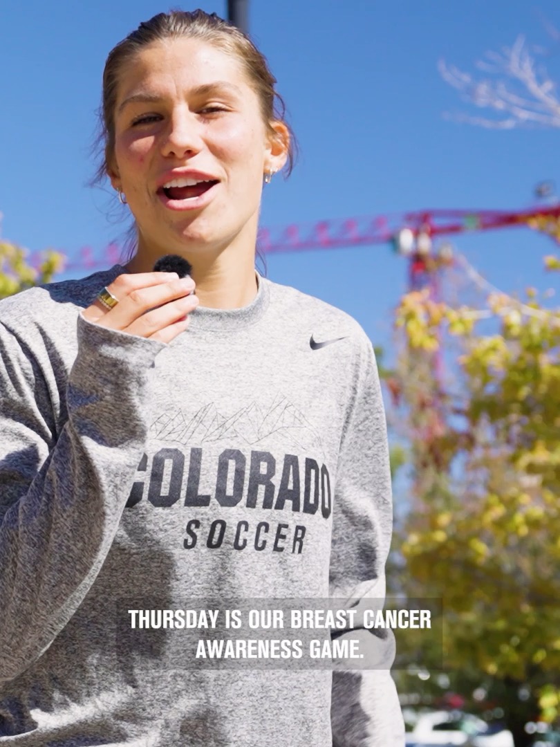 A young woman wearing a gray 'COLORADO SOCCER' Nike sweatshirt speaks outdoors with the caption 'THURSDAY IS OUR BREAST CANCER AWARENESS GAME.' overlaid at the bottom.