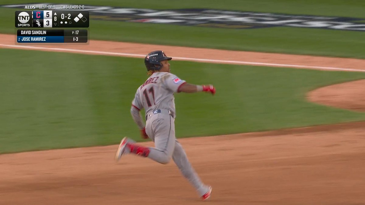 A Cleveland Guardians baseball player in a gray uniform is captured mid-stride rounding the bases, with the number 11 and a partially visible name on his back. The TNT Sports scoreboard shows Cleveland leading Chicago 5–3 in the 8th inning with an 0–2 count, and lists “DAVID SANDLIN” as pitcher and “2 JOSE RAMIREZ” as the batter.