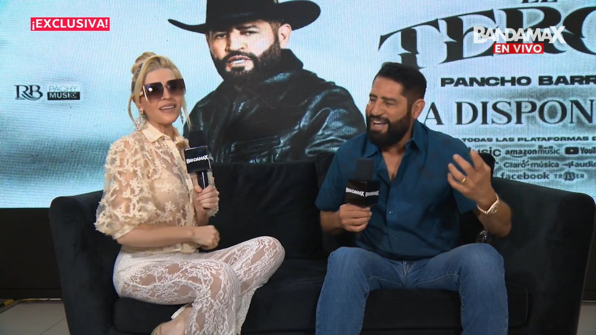 A blonde woman in a lace outfit interviews a bearded man in a blue shirt on Bandamax, with promotional posters for 'EL TROG' and 'PANCHO BARRAZA' behind them.