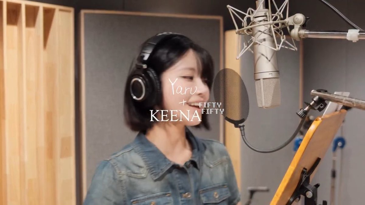 A woman wearing headphones and a denim shirt smiling in a recording studio in front of a professional microphone, with text overlay reading 'Yaru + KEENA' and 'FIFTY FIFTY'.