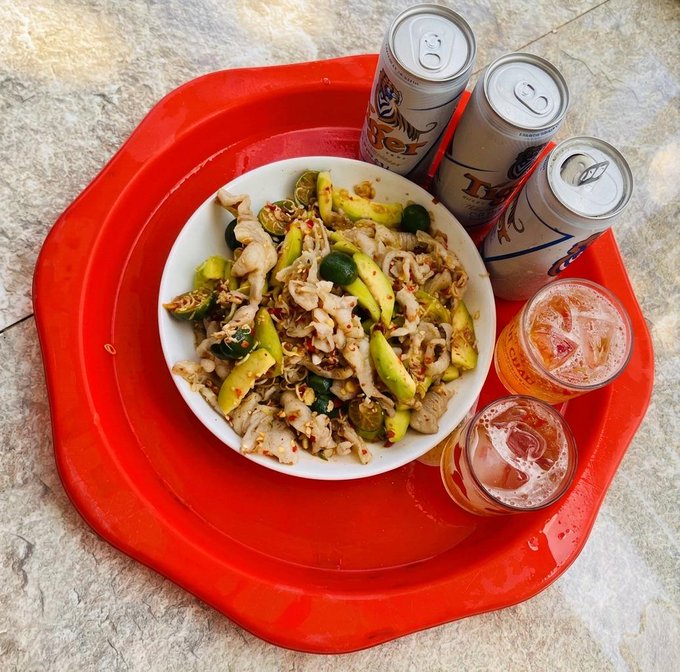 An overhead view of a red tray holding a bowl of mixed food with vegetables and meat, accompanied by three Tiger brand beer cans and two glasses of iced beer.