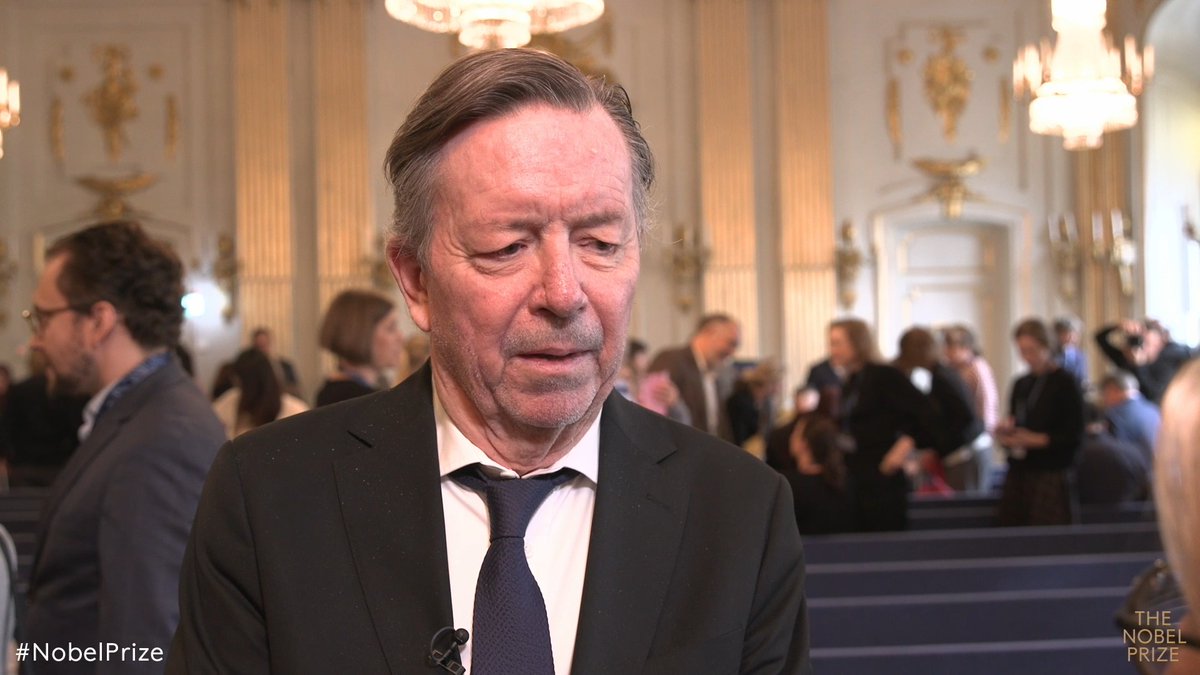 The image shows Steve Sem-Sandberg, a member of the Swedish Academy, being interviewed in an ornate hall during the 2026 Nobel Prize announcement, as indicated by the "#NobelPrize" and "THE NOBEL PRIZE" text visible in the corners of the frame.
