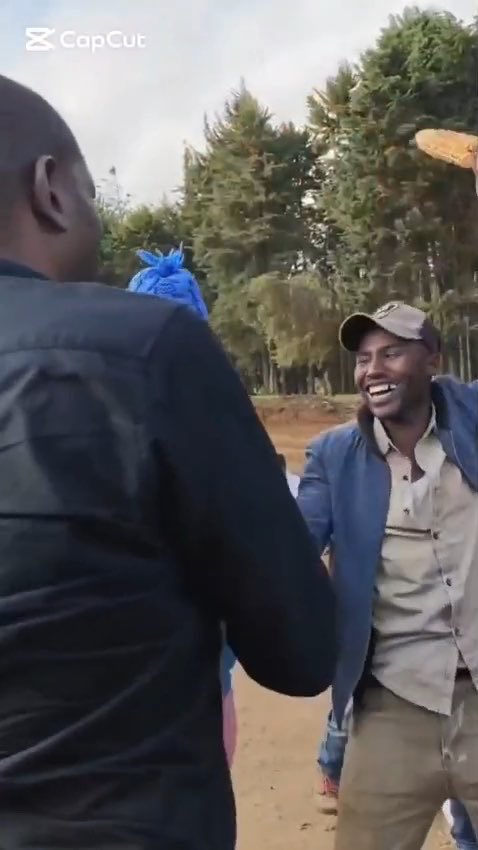 Video still showing a smiling man in a blue jacket and cap outdoors in a wooded area, edited with CapCut.