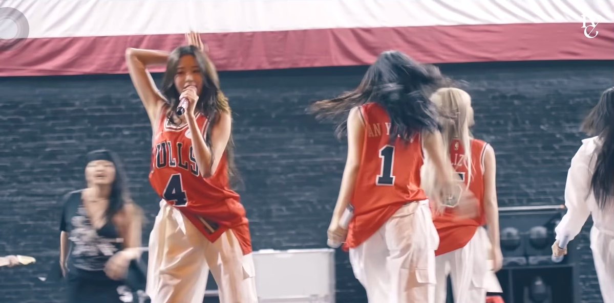 Female performers in red Chicago Bulls basketball jerseys and white pants perform on stage, with one in a #4 jersey singing into a microphone while dancing.