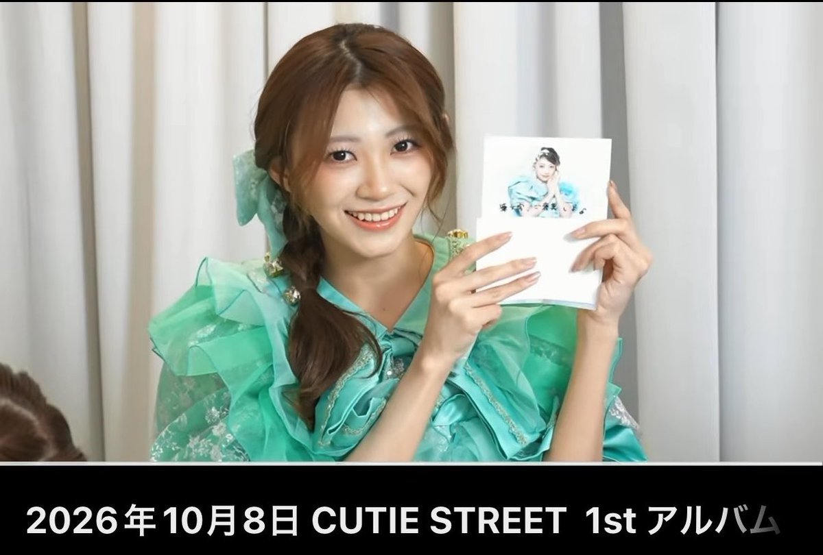 A young woman with a side braid wearing a mint green ruffled outfit, smiling while holding a polaroid-style photo, with text reading '2026年10月8日 CUTIE STREET 1st アルバム'.