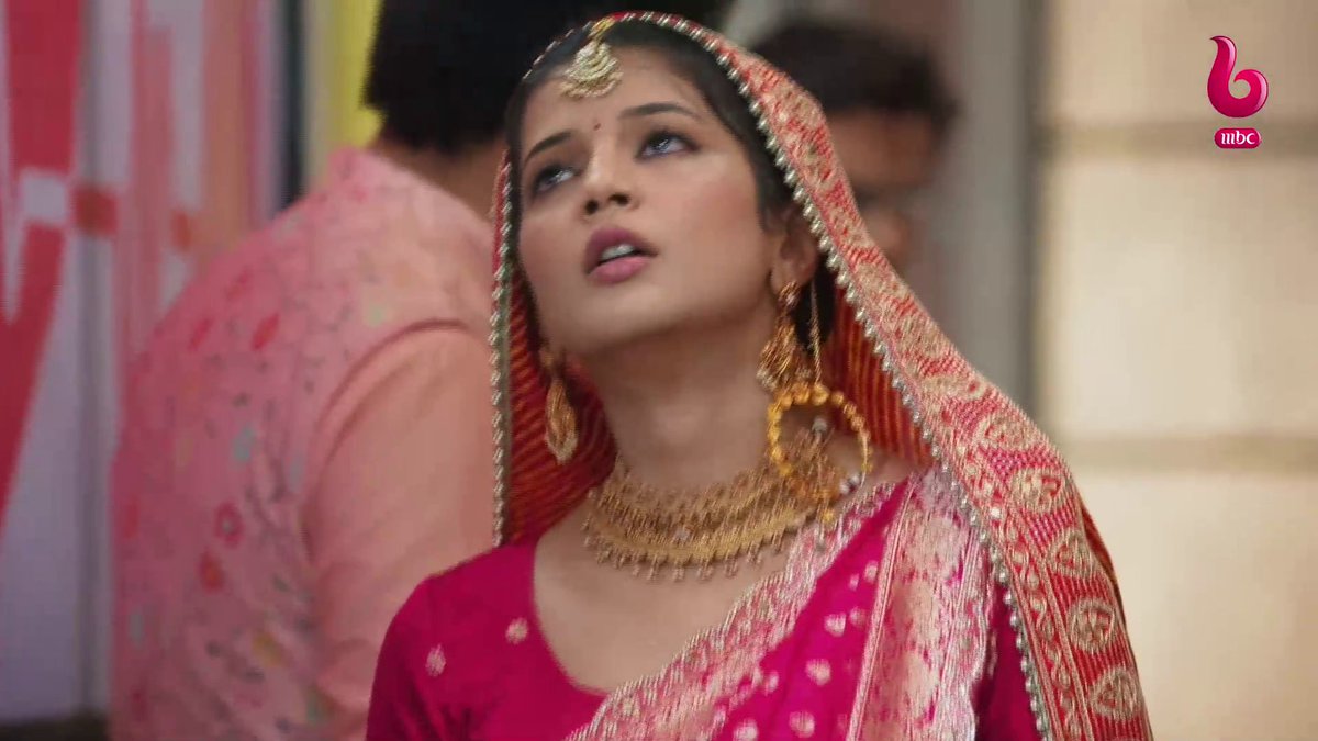 A still from a TV show featuring a woman in traditional South Asian bridal attire, wearing a red and gold embroidered sari, heavy gold jewelry, and a nose ring, with an 'mbc' logo in the corner.