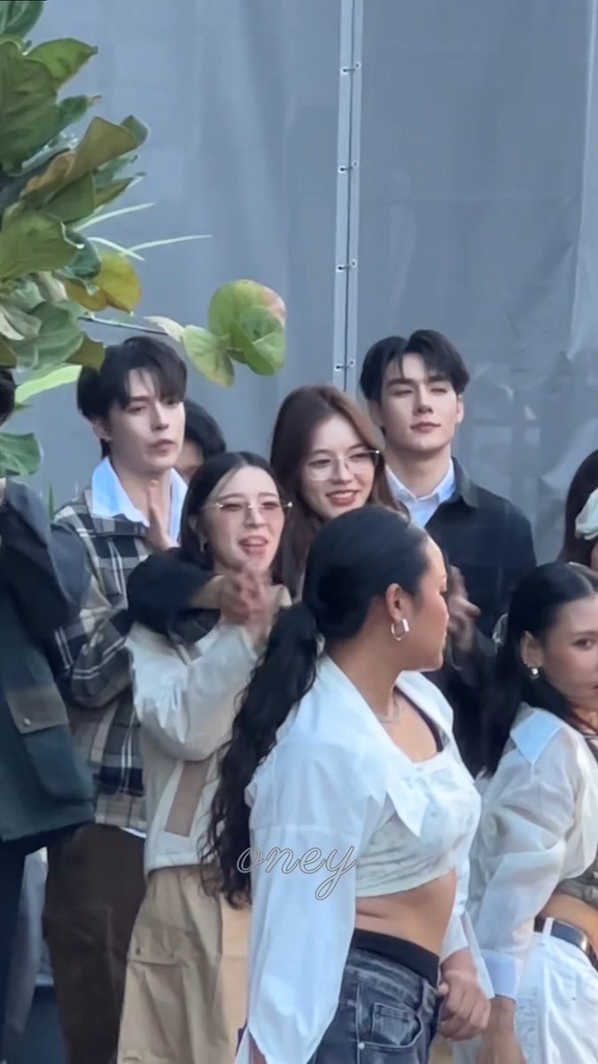 A group of young people, mostly dressed in white and plaid, pose together outdoors with plants in the background; the image is watermarked "@meyy".
