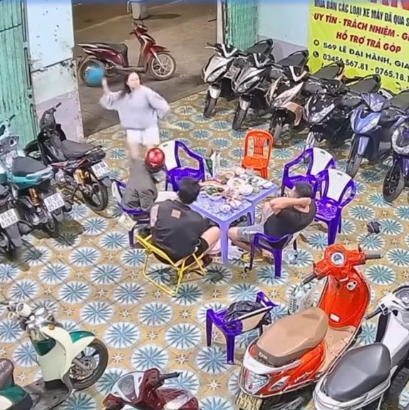An overhead view shows a group of people sitting around a table with food and drinks outside, surrounded by parked motorbikes on a tiled surface.