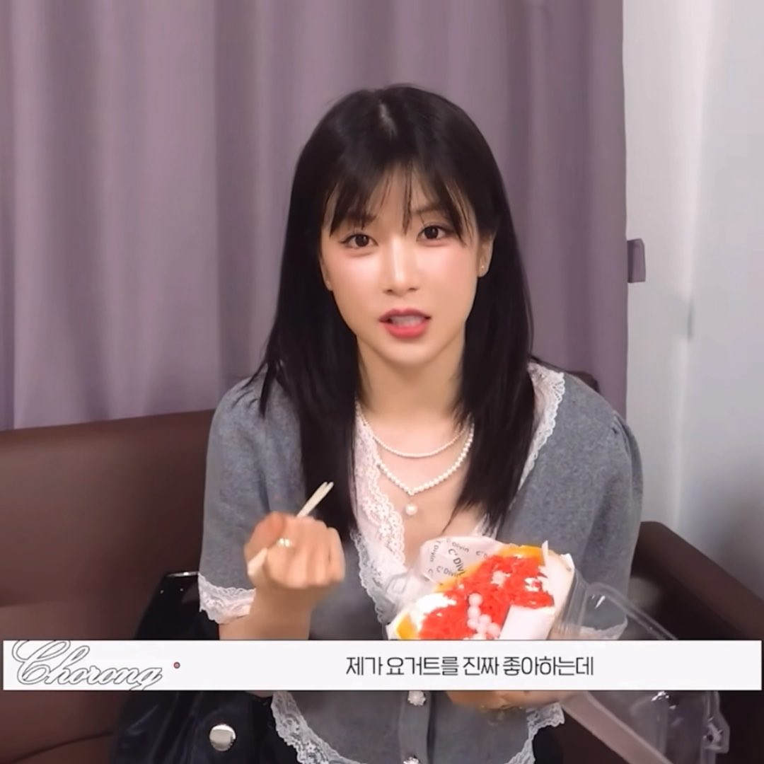 A video screenshot of a woman with dark hair holding a dessert topped with red fruit, with Korean subtitles reading '제가 요구트를 진짜 좋아하는데' and a 'Chorong' logo.