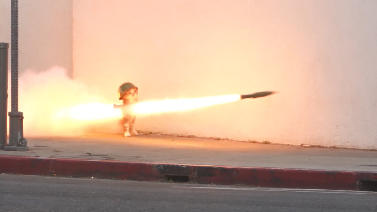 A soldier wearing a helmet fires a shoulder-mounted rocket launcher, with a dramatic burst of flame and smoke engulfing the scene.