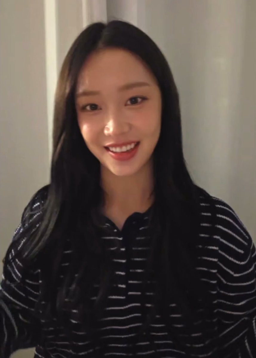 A young woman with long dark hair wearing a black and white striped sweater smiles brightly at the camera.