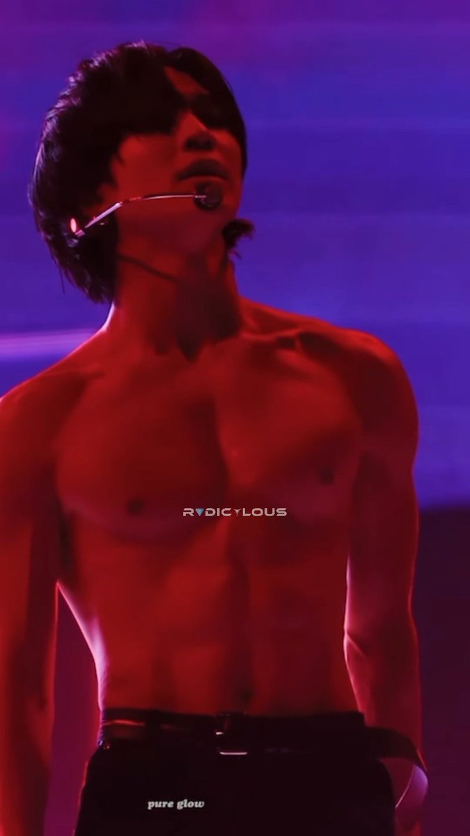 A shirtless male performer with dark hair and a headset microphone stands on stage under red lighting, with watermarks 'RADICULOUS' and 'pure glow' visible.