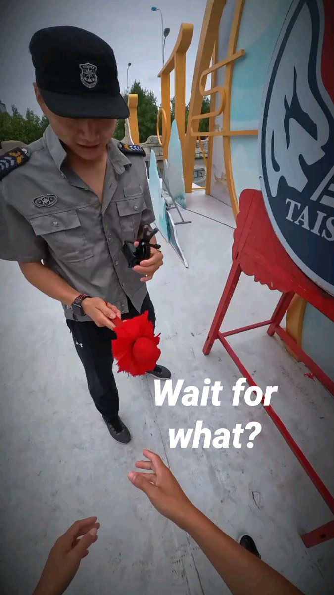A man wearing a security guard uniform and cap holds a small red hat, looking at a person reaching out, with 'Wait for what?' text overlaid and a 'TAISHAN' logo visible.
