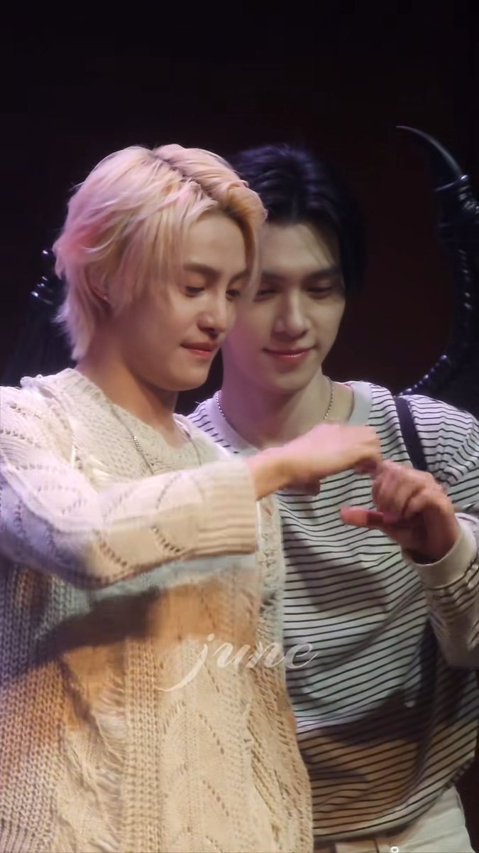 Two young men, including one with pink-dyed blonde hair wearing a cream knit sweater, are shown performing a pinky promise gesture, with a watermark reading 'june' across the image.