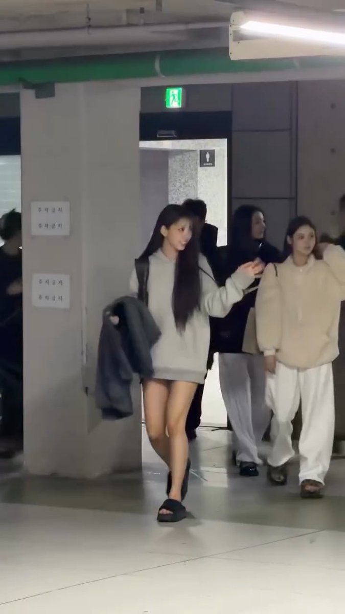 The post mentions "#미야오 #MEOVV," referencing the K-pop group MEOVV and its member Miyaw, who appears in the image as the young woman with long dark hair wearing an oversized gray sweater dress and carrying a jacket while walking through what looks like a backstage or studio hallway.