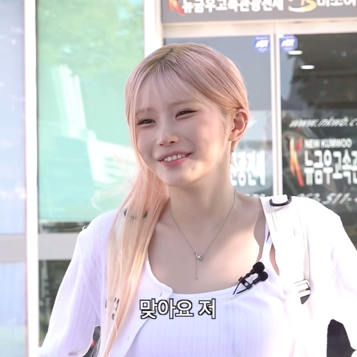 A close-up photo shows a smiling young woman with blonde hair tied back, wearing a white top and a delicate necklace. Korean text '맞아요 저' is overlaid at the bottom, with Korean storefront signage visible in the blurred background.