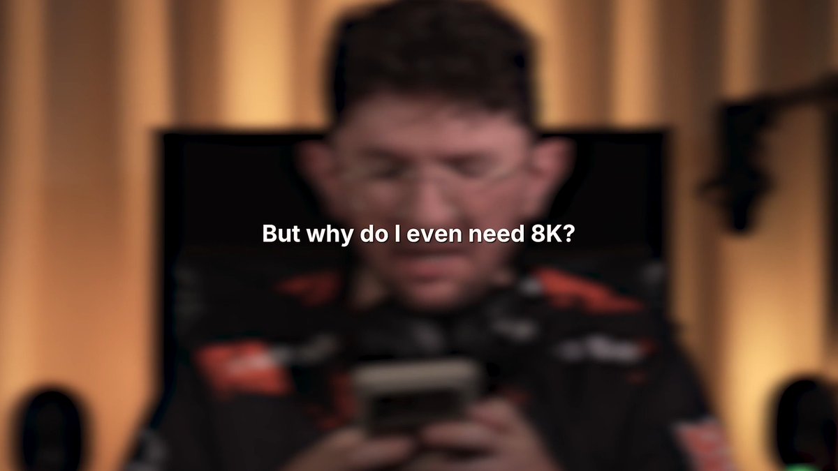 A blurred man looks at a smartphone while the text "But why do I even need 8K?" appears on screen. The intentionally blurry image humorously illustrates the post's point about 8K polling, implying that users won't even be able to clearly see the person on their screen without such high-resolution features.