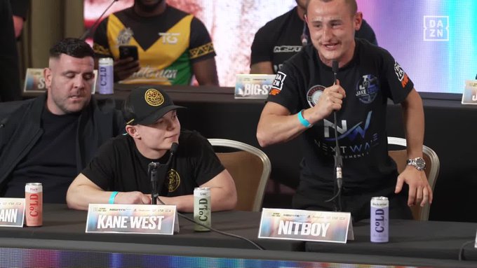 A press conference scene shows two men seated at a table with name placards reading "KANE WEST" and "NITBOY," with the man on the right speaking into a microphone while wearing a black "NEXTWAVE" shirt. Cans of "COLD" beer are visible on the table, and the "DAZN" logo appears in the upper right corner, tying into the broadcast promo for the EssexDapper event featuring Nitboy, Little T, and Cracky Tokky.