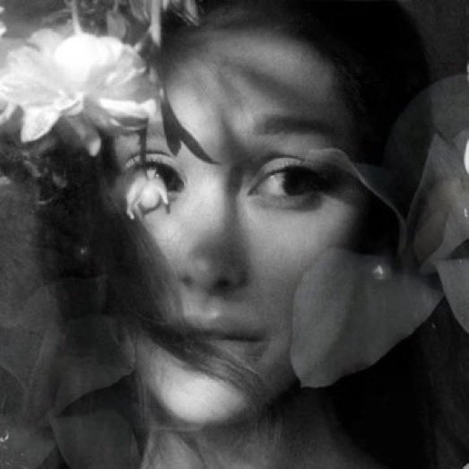 A black and white double-exposure portrait of a young woman's face blended with floral elements, giving the image an ethereal, dreamlike quality.