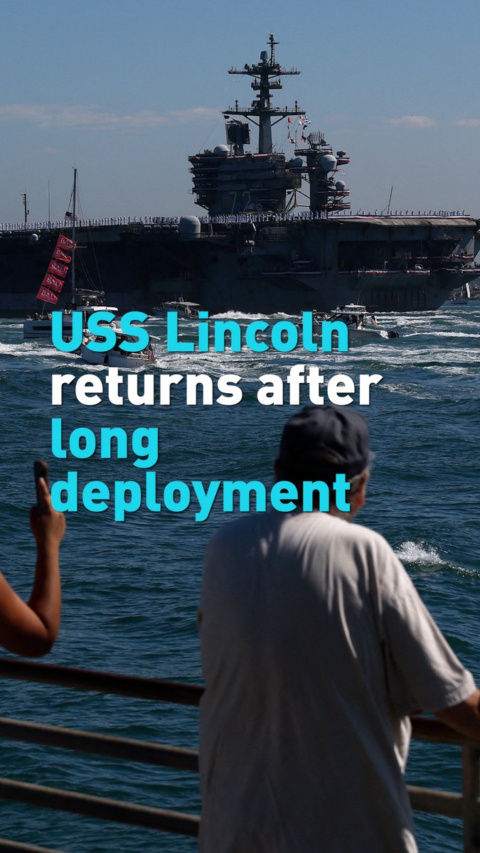 A photograph of a massive aircraft carrier at sea with people lined along the deck, while a person in the foreground watches from a pier, with cyan text overlay reading 'USS Lincoln returns after long deployment'.