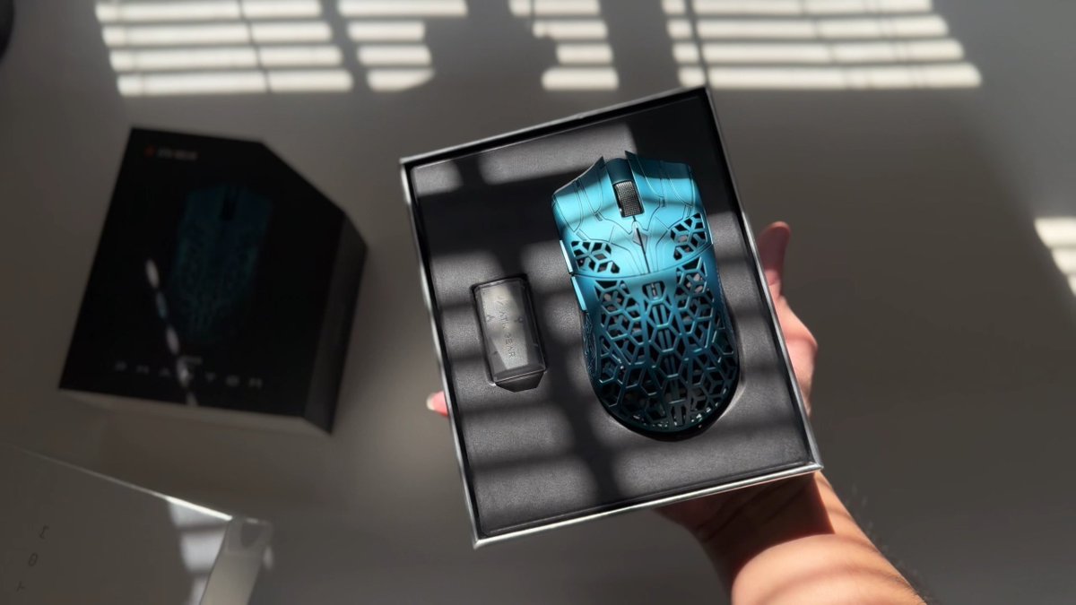 A hand holds an open ATK-branded box revealing a teal-blue gaming mouse with an intricate honeycomb/lattice shell design alongside its USB receiver, set against a backdrop of dramatic slatted window shadows. The aesthetic presentation reinforces the post's "Phantom" branding, positioning ATK as a sleek, shadowy rival to FinalMouse in the ultralight gaming peripheral space.