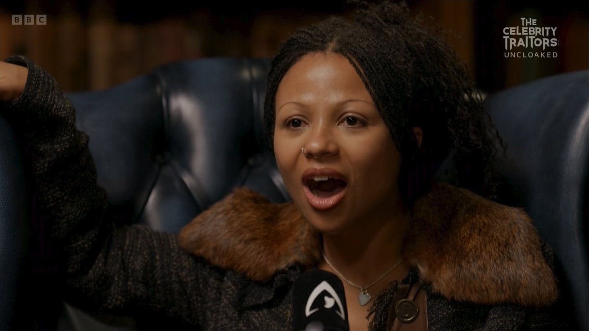Myha'la sits in a blue leather chair with her mouth wide open in shock, wearing a dark coat with a fur collar, as she reacts to learning the identities of the Traitors. The BBC logo and "The Celebrity Traitors: Uncloaked" title are visible in the top corners, matching the post's reference to her surprise reveal moment on #Uncloaked.