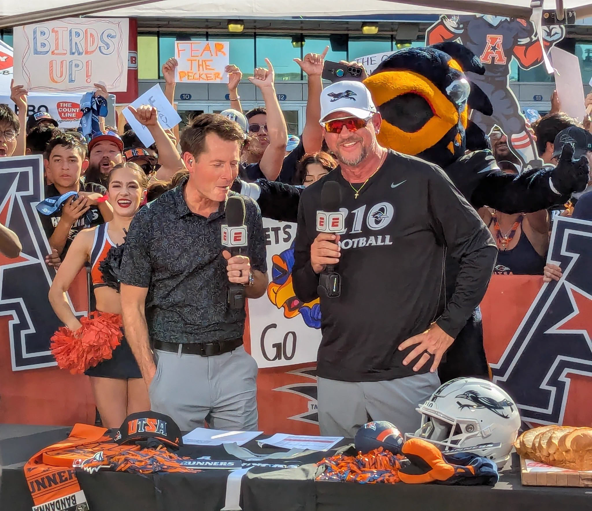 Matt Barrie and Jeff Traylor have an interview while fans cheer in the back.