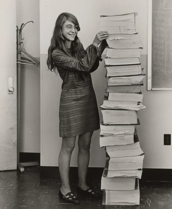Margaret Hamilton standing beside a massive stack of source code printouts