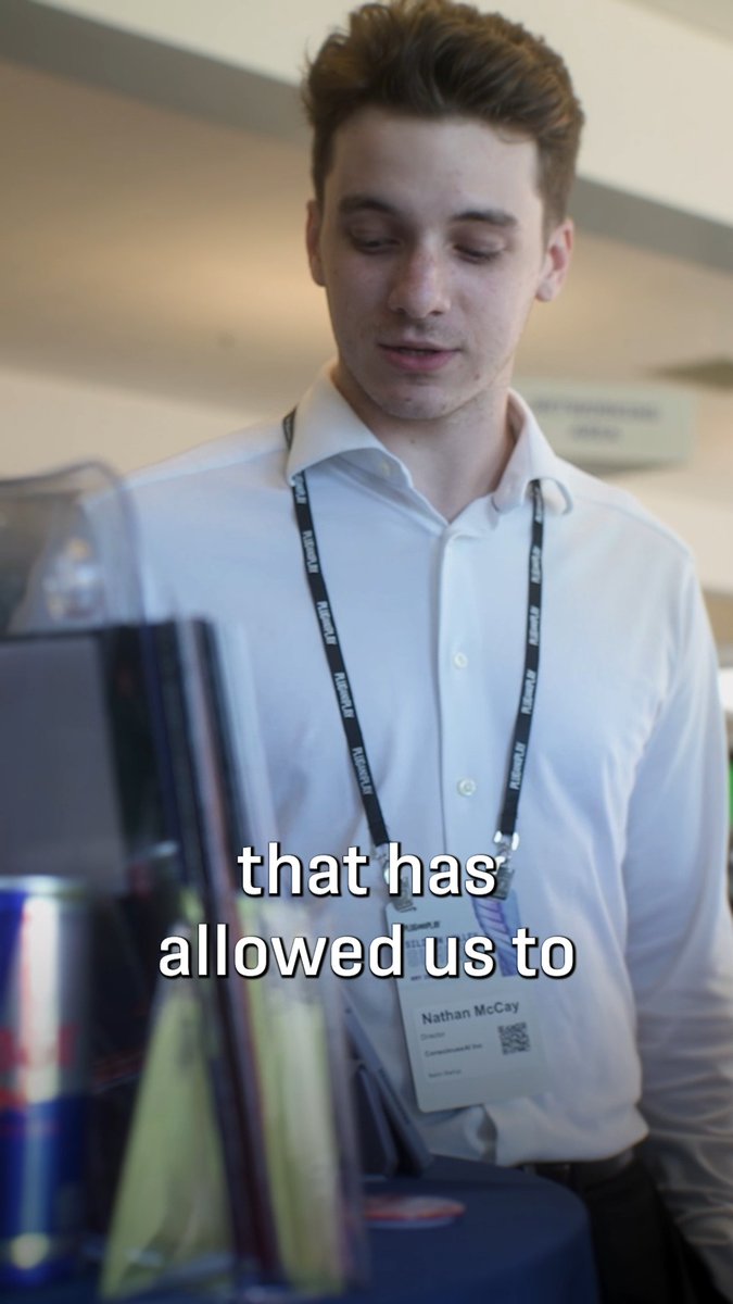 A young man named Nathan McCay, wearing a white shirt and a 'TEAM UK' lanyard with his ID badge, looking down in what appears to be a convention or expo setting, with the subtitle text 'that has allowed us to' visible on screen.